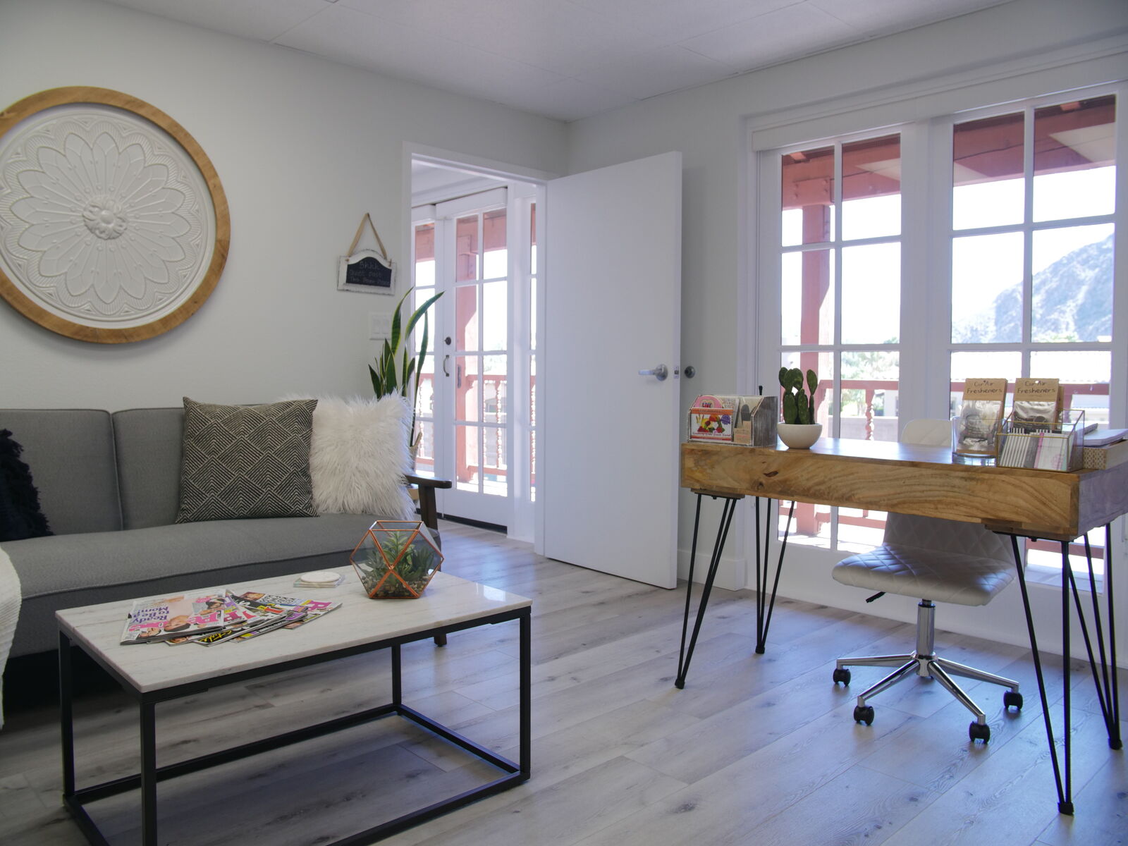 Bright waiting lounge with a grey sofa, wood desk and mountain views through French doors