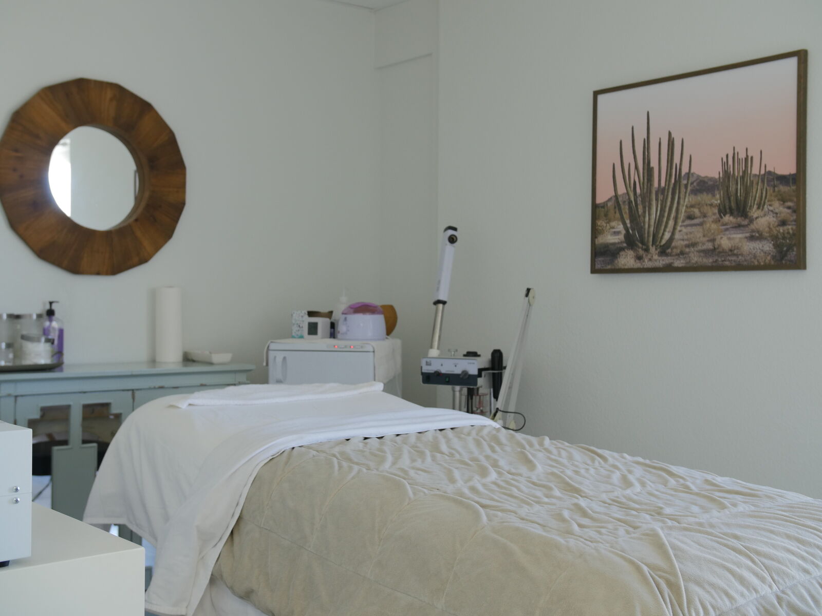 Treatment room with a made-up facial bed, warm towel cabinet and desert artwork
